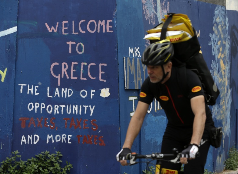 A courier with his bicycle passes graffiti on a wall in Athens, Friday, April 21, 2017. Greece’s independent statistics agency says the country has posted a high primary budget surplus in 2016, at 3.9 percent of gross domestic product. (AP Photo/Thanassis Stavrakis)